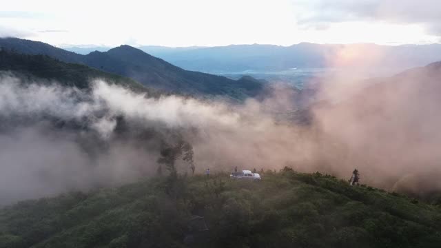 阴天日出时，无人机鸟瞰站在山顶上的游客群。全景绿色森林与风吹雾海的雾通过山脉在泰国清迈视频下载