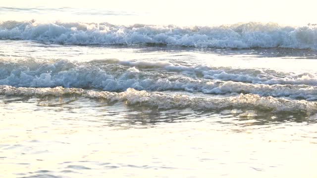 4 k决议。明亮的阳光在水面和波浪在早晨的光波慢慢地打破海岸上的热带白色沙滩与暖色反射。视频素材