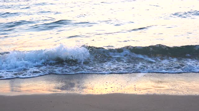 4 k决议。明亮的阳光在水面和波浪在早晨的光波慢慢地打破海岸上的热带白色沙滩与暖色反射。视频素材