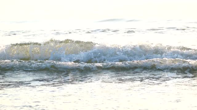 4 k决议。明亮的阳光在水面和波浪在早晨的光波慢慢地打破海岸上的热带白色沙滩与暖色反射。视频素材