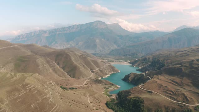 风景如画的吉日吉特蓝湖位于山沟峰顶景观。无人机在巴尔卡里亚的棕色山脉中拍摄令人惊叹的湖泊。湖岸边高地上的汽车路。视频素材