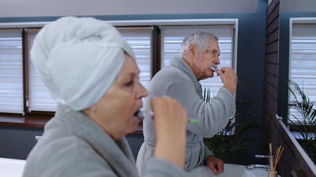 老夫妇奶奶和爷爷一边刷牙，一边在浴室里照镜子视频素材