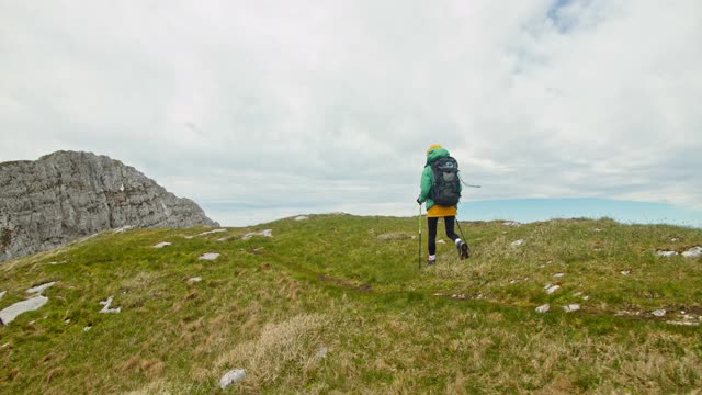 一个年轻的背包客拄着拐杖走在山顶上视频素材