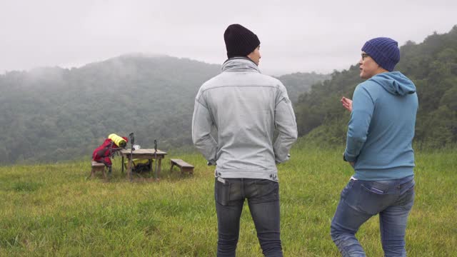 两名亚洲男子在冬日的森林山徒步旅行。快乐的背包客朋友坐在户外的椅子上，一起享受聊天。友谊和户外度假概念。视频素材