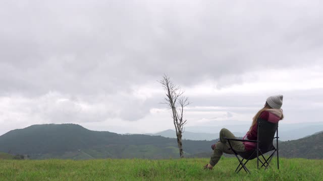 4K快乐年轻的亚洲女性游客坐在户外的椅子上放松在美丽的自然森林山和草地在冬天的一天。漂亮的女孩喜欢在假期的户外生活方式。视频下载