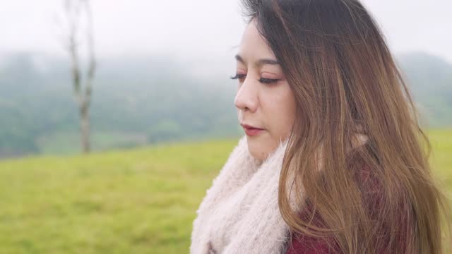 孤独亚洲女人独自站在草地上，在雾蒙蒙的冬日。美丽的女孩看美丽的森林山的自然。户外生活方式和假日度假概念。视频素材