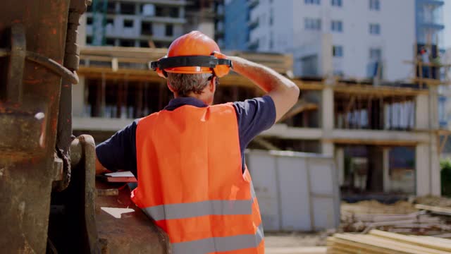 成熟的男建筑工人在建筑工地上看着建筑，他戴着安全帽视频素材