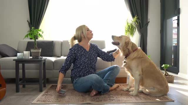 美丽的女人与她可爱的金毛猎犬在家里玩得开心。视频素材