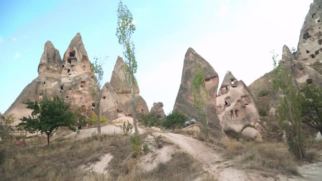 手持，低角度的视角，在Uchisar洞穴城市旅行，乡村古卡帕多西亚景观与stock形成的山脉作为一个小村庄和一个教堂在蓝天下。火山和乡村生活的概念。视频素材