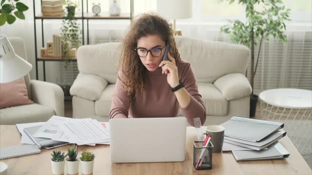 在办公室工作时使用手机和笔记本电脑的女性视频素材