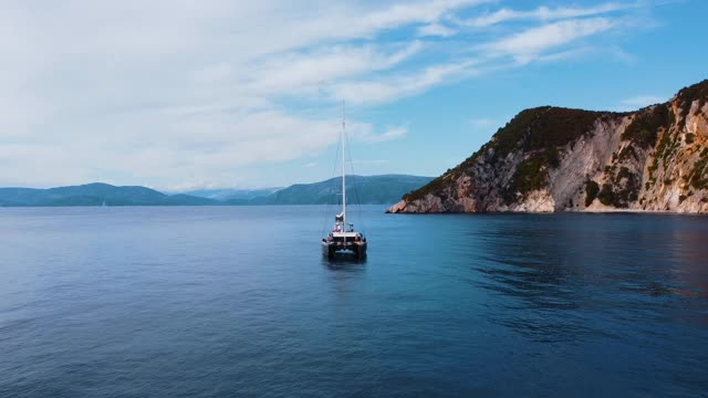 帆船停泊在蓝色平静的海面上，背景是雄伟的山脉视频素材