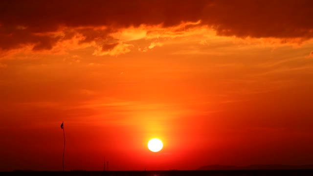 海面上的夕阳和剪影的旗帜摇摆着黑暗的天空时间流逝视频素材