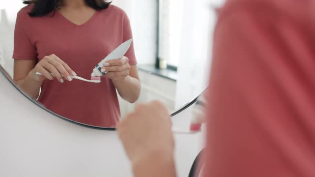 特写的女人的手挤牙膏刷在浴室准备清洁她的牙齿视频素材