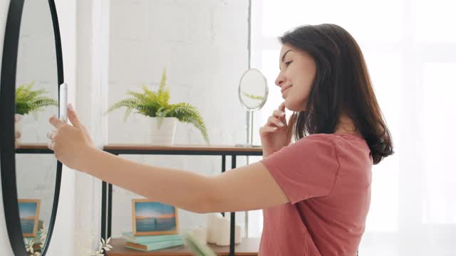 年轻的黑发女子用智能手机摄像头在浴室镜子里自拍视频素材