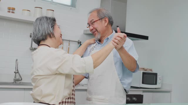 夫妇老亚洲长者幸福生活在家庭厨房。爷爷奶奶跳着幸福的舞蹈，微笑着享受退休生活。老年人的家庭关系和活动概念。视频素材