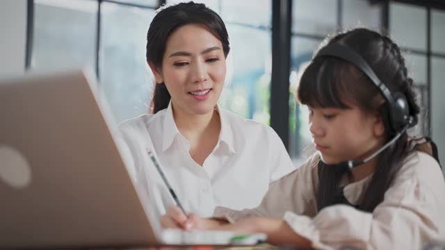 亚洲家庭一起在家学习。小女孩和妈妈在客厅学习教育班。女人和孩子笑和感觉乐趣，享受学习和玩科目在电脑笔记本电脑。视频素材