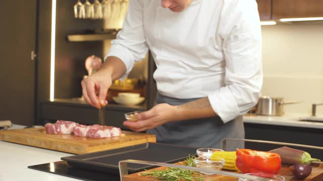 烧烤肉排食谱。厨师洒香料新鲜生肉牛排在现代餐厅厨房。烹饪上准备美味的食物。男人们在烧烤咖啡馆做饭。烤盘的食物视频素材