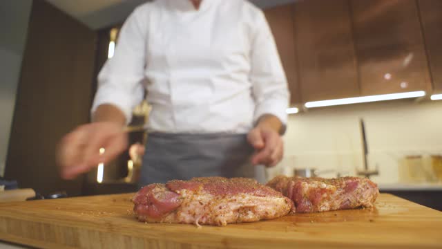 烧烤肉排食谱。厨师洒香料新鲜生肉牛排在现代餐厅厨房。烹饪上准备美味的食物。男人们在烧烤咖啡馆做饭。烤盘的食物视频素材