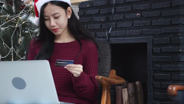 年轻的亚洲女性网购用信用卡在笔记本电脑上，女性购物用借记卡支付，圣诞节在过节，新年快乐，顾客用购物到网上。视频素材