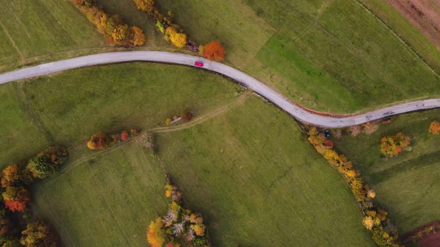 穿过草地和田野的单车道乡村公路上行驶的红色汽车视频素材