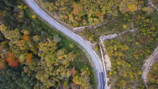 无人机对一辆在秋季蜿蜒乡村道路上行驶的汽车的看法视频素材