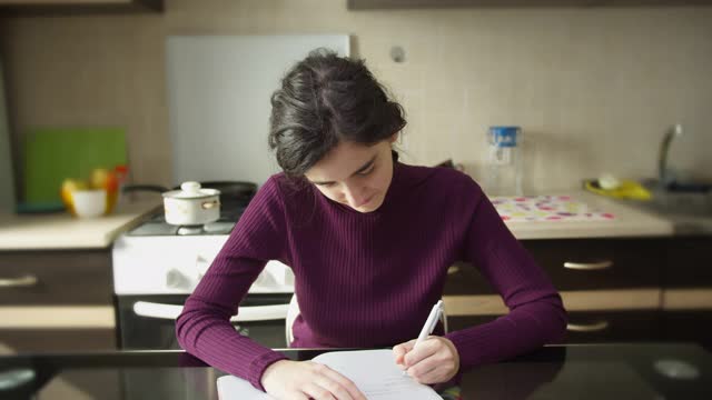 可爱的女学生坐在餐桌旁，在笔记本上做笔记视频素材