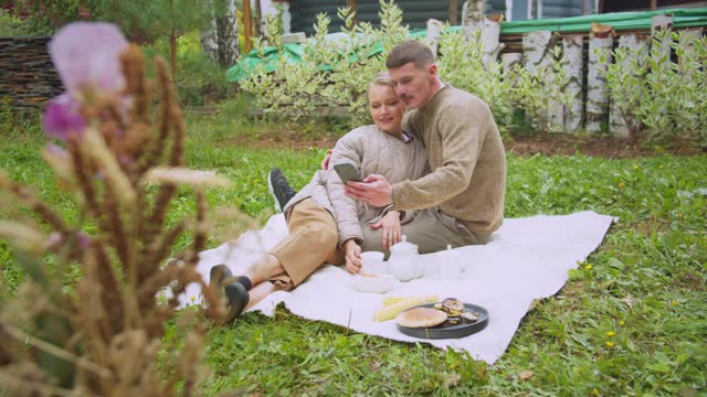 一对斯拉夫夫妇在村庄的院子里野餐，用智能手机自拍视频素材