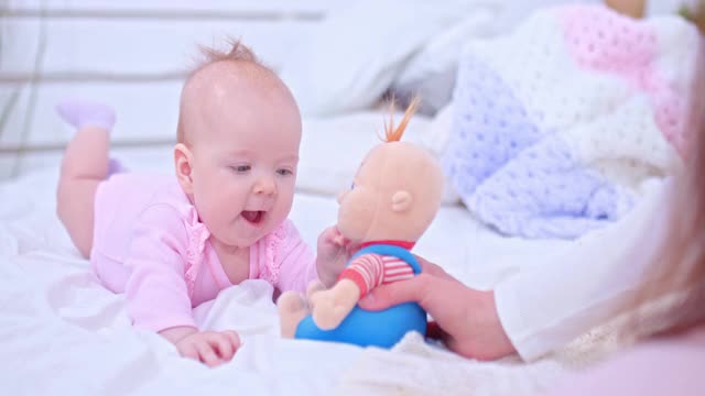 美丽的新生婴儿躺在床上玩玩具。新生的小女孩趴在地上，用手去抓洋娃娃。4 k, ProRes视频素材