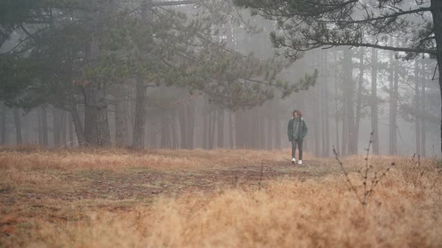 一个背着双肩包的年轻女子走在迷雾笼罩的森林里的一条小路上视频素材