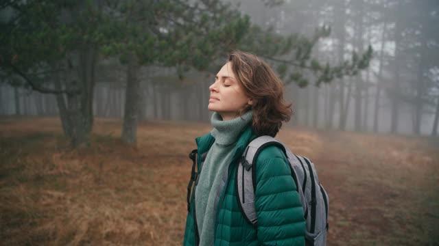 一位快乐的年轻女子在薄雾弥漫的森林里散步，呼吸着新鲜空气视频素材