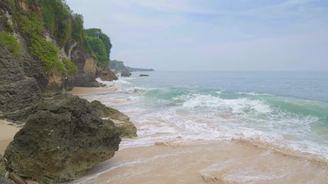 全景热带海滩与岩石在左边和沙子和大浪在蓝色和绿色的海洋与地平线视频素材