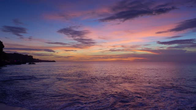 岩石海滩与高悬崖和紫色日落在海洋视频素材