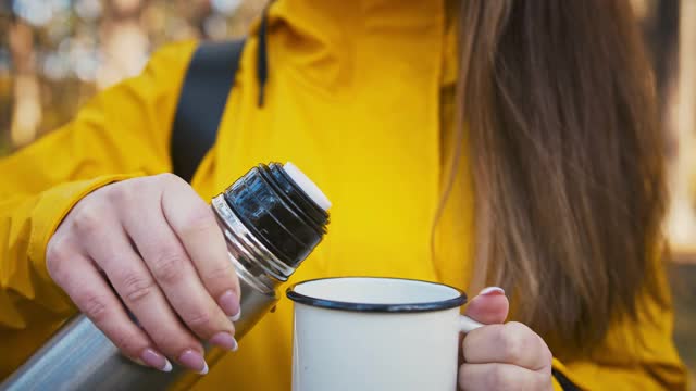 一名穿着大衣背着背包的不明女性正在把热茶从保温瓶里倒进杯子里视频素材