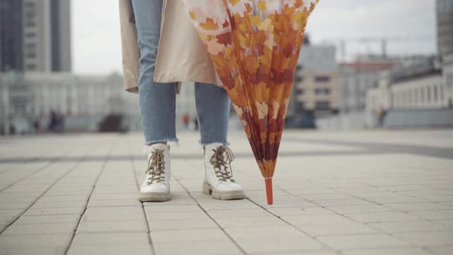 一个陌生的年轻女子站在城市广场上，撑着伞，纺纱。无忧无虑的白人女士在雨阴天的春天或秋天在户外等待视频素材