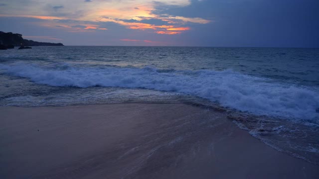 热带海滩在黑暗的夜晚与高浪潮附近的岩石和蓝色与橙色的日落天空视频素材