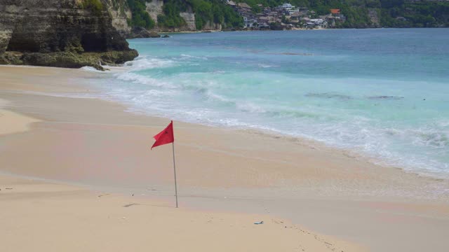 炎热的天气里，热带海滩上的大浪正在缓慢地挤压沙子，海滩上挂着红色游泳禁止旗，海水中有塑料和有机垃圾视频素材