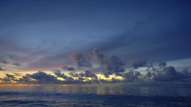 美丽的全景，一个平静的海与大的蓝色波浪附近的海滩日落后与云在黄色和紫色的天空反射在水视频素材