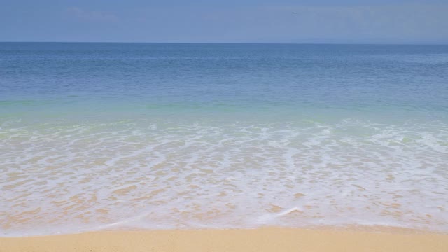 蔚蓝的海洋与巨大的温暖的海浪和浪花从沙滩下干净的蓝色天空和飞机降落在背景视频素材