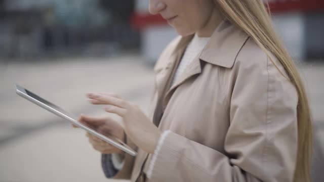 一个陌生的年轻女性在户外用平板电脑发信息。自信的现代白人女士上网或滚动网页站在多云的城市广场视频素材