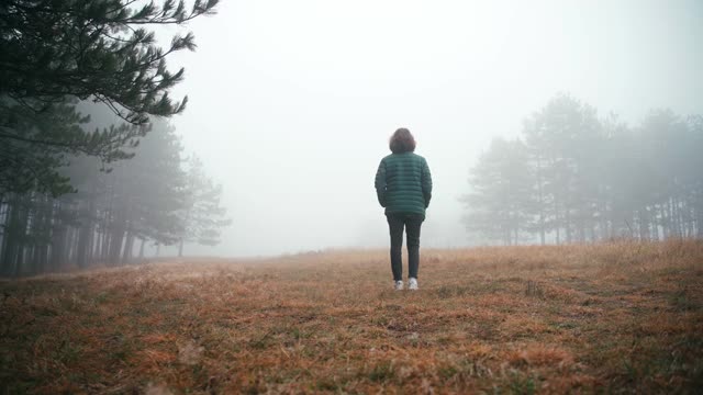 一个年轻的女人在一个雾蒙蒙的秋天的森林空地上的电影镜头视频素材