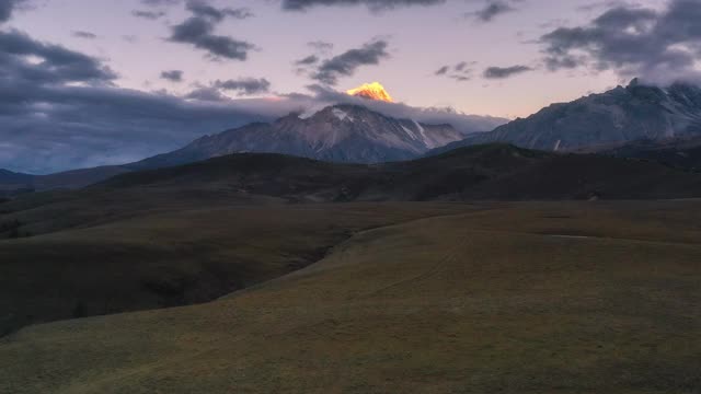 连绵不断的草原后面，雪山的山顶被日出的光芒所照亮视频素材