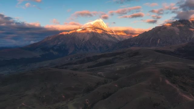 连绵不断的草原后面，雪山的山顶被日出的光芒所照亮视频素材