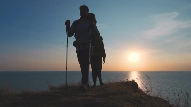 一男一女背着背包走在海边的山上。慢动作视频素材