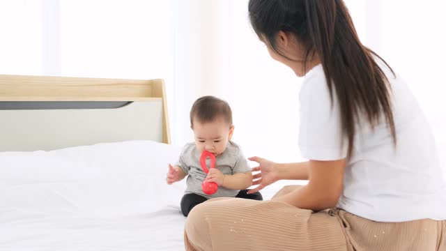 亚洲新生女婴抱着并嚼着柔软的橡胶和妈妈玩她的宝宝。视频素材