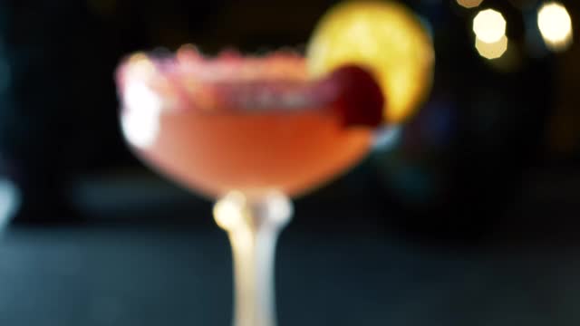 特写跟踪镜头的一个清爽的红色鸡尾酒在酒吧和一个女性的手装饰水晶玻璃与一朵花视频素材