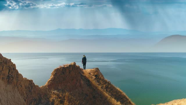 游客带着包站在山边，以海景为背景视频素材