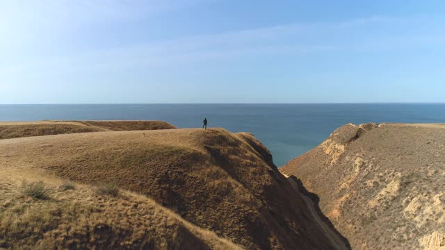 那个背着背包的人站在山顶上，背对着海景视频素材