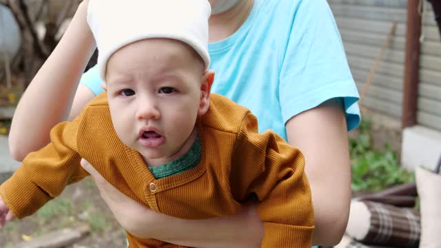 在一个阳光明媚的夏日，幸福的一家人在户外散步。一位慈爱的母亲把年幼的儿子抱在怀里视频素材