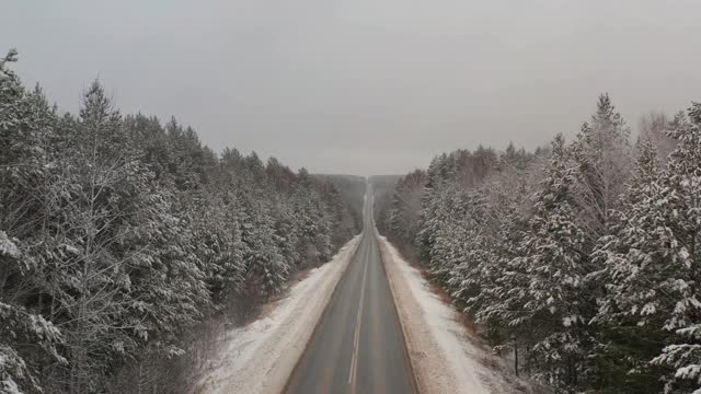 汽车行驶在积雪覆盖的轨道上，俯视图。冬天的路在寒冷的清晨在冰冻的密林之间穿行视频素材