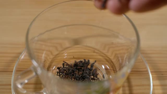 男子将干红茶倒进木桌上的玻璃杯中。温暖柔和的光线，较暗的背景。新鲜冲泡的红茶在透明的玻璃杯。茶点仪式禅宗放松。视频素材